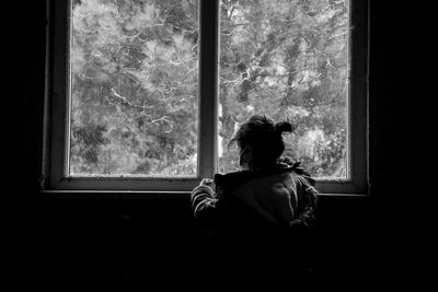 Rear view of woman looking through window at home