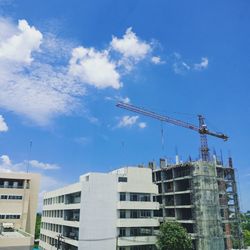 Low angle view of crane by building against sky