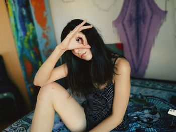 Portrait of young woman gesturing while sitting on bed at home