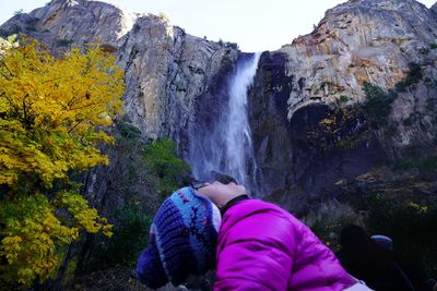 Rear view of waterfall amidst rocks against trees