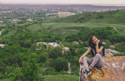 Young woman sitting on grassland against trees