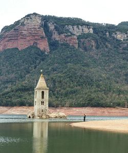 Man standing by church at lakeshore against mountain