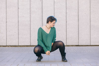 Full length of young woman sitting on wall