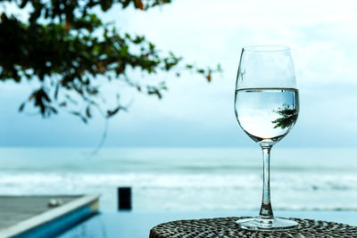 Glass of water on table by sea against sky