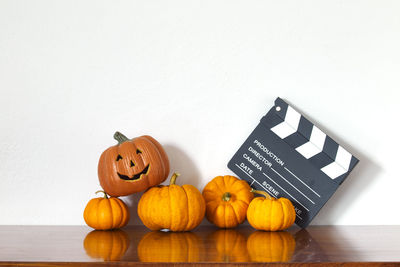 Jack o lantern with pumpkins and film slate on table against white wall