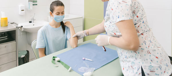 Midsection of doctor taking blood sample from patient