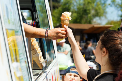 Cropped hand giving ice cream to girl from van