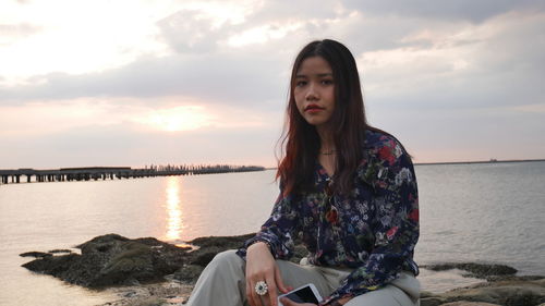 Portrait of woman sitting on beach against sky during sunset