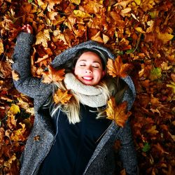 Smiling young woman with closed eyes lying down on autumn leaves