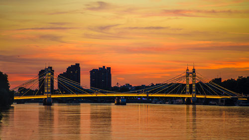 Suspension bridge over river against cloudy sky during sunset