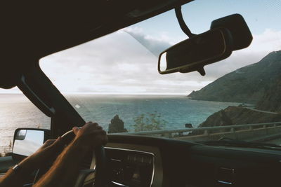Cropped hand of man driving car on road by sea