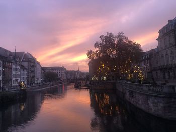 Bridge over river in city against sky at sunset