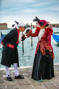 Couple in costume standing at harbor during venice carnival