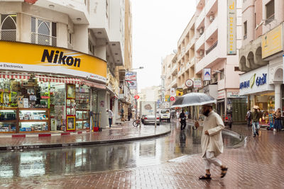 People walking on wet street against buildings in city