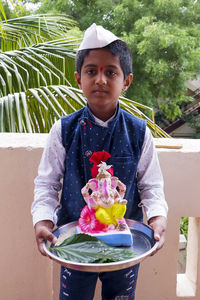 Portrait of boy holding ganesh statue standing at balcony