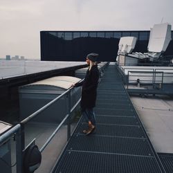 Smiling young woman standing on bridge against sky