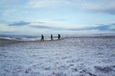 People walking on field against sky during winter