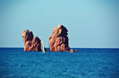 View of rock formation in sea against clear blue sky