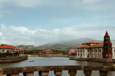 Buildings at waterfront against cloudy sky