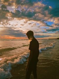 Man standing on beach against sky during sunset