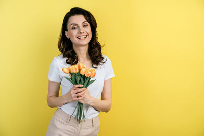 Portrait of a smiling young woman standing against yellow background