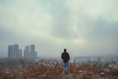 Rear view of man standing by cityscape against sky