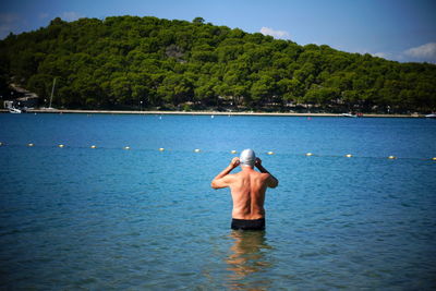 Rear view of shirtless man standing in sea against sky