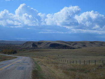 Empty road amidst field against sky