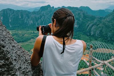 Rear view of woman photographing nature against mountains