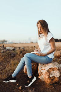 Mid adult woman sitting on field against clear sky