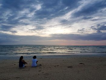 Rear view of men sitting on beach against sky