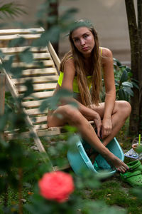 Portrait of young woman sitting on field on a garden chair and keeps his feet in the basin