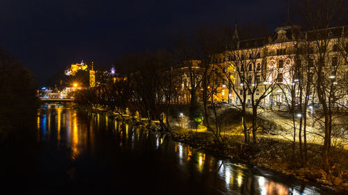 Illuminated bridge over river by buildings in city at night