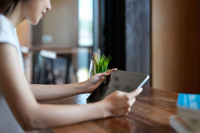 Midsection of woman using digital tablet while sitting on table