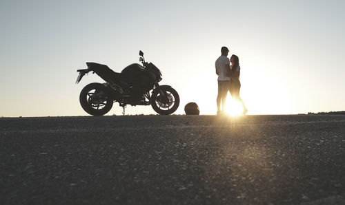 Backlighting of a couple posing on the road with their motorcycle