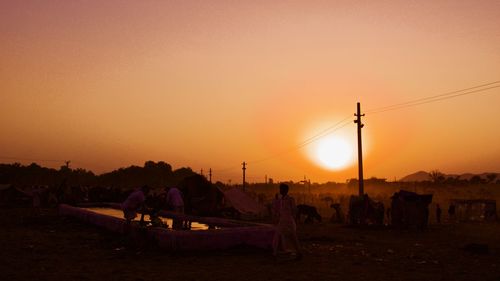 Silhouette people on field against sky during sunset