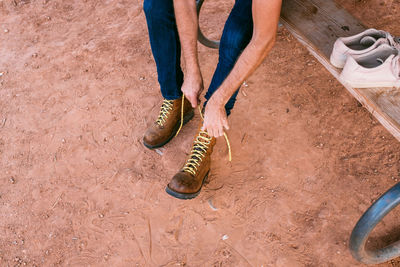 Low section of person tying shoelace on mud