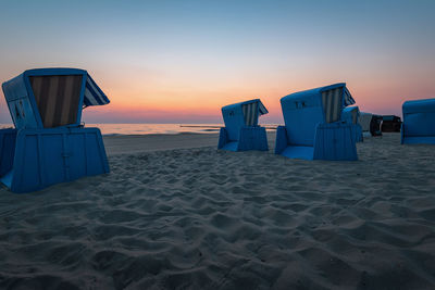 Hooded beach chairs on shore against sky during sunset