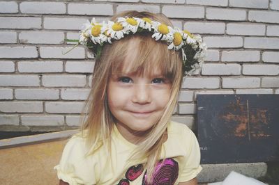 Close-up portrait of girl wearing flowers by wall