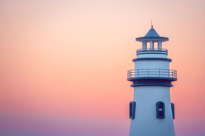 Lighthouse by sea against orange sky