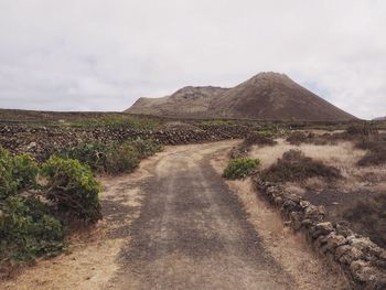 Dirt road amidst landscape against sky