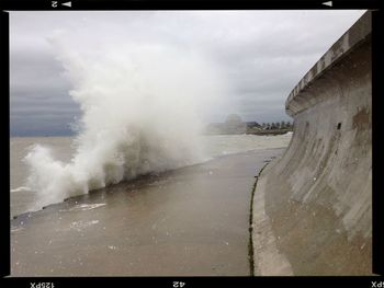 Waves splashing in sea against cloudy sky