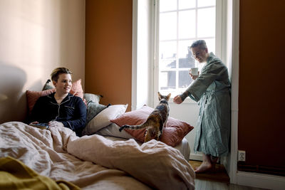 Lesbian couple spending leisure time with cat in bedroom at home