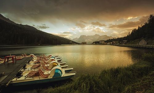 Paddleboats moored on lake misurina against cloudy sky during sunset