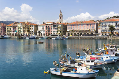 Sailboats moored in harbor by buildings in city against sky