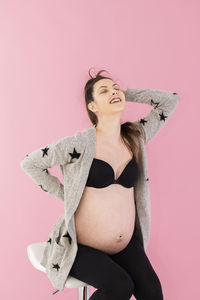 Woman with arms raised standing against pink background