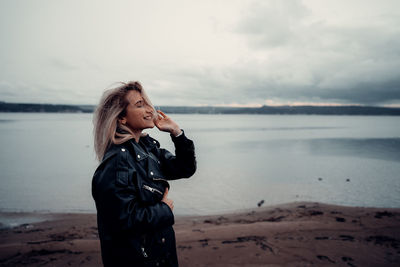 Young woman standing at beach against sky