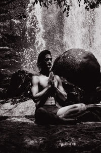 Young woman doing yoga against waterfall