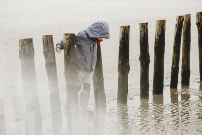 Full length view of boy leaning on pilings on a cold winter beach