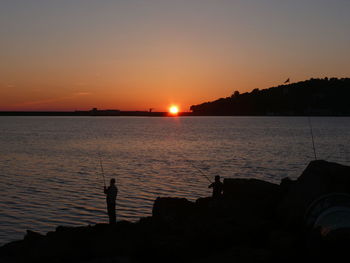 Silhouette man fishing in sea against clear sky during sunset